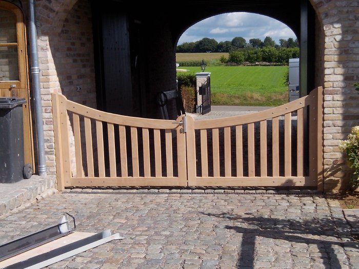 Een maatwerk houten tuinpoort in een landelijke omgeving.